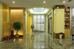 Un vestíbulo de hotel con piso de mármol, una recepción, una planta y una estantería.