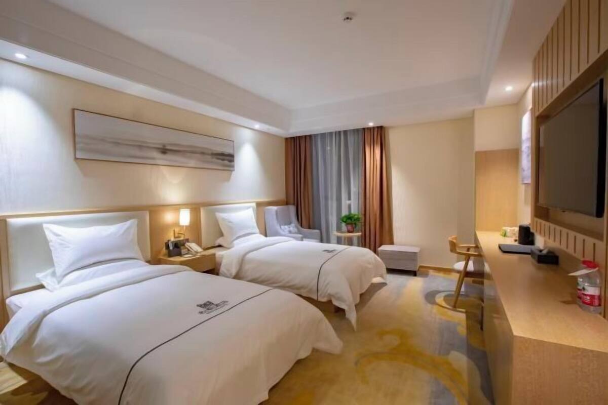 A hotel room with two beds, a desk, a chair, a TV, and a painting on the wall.