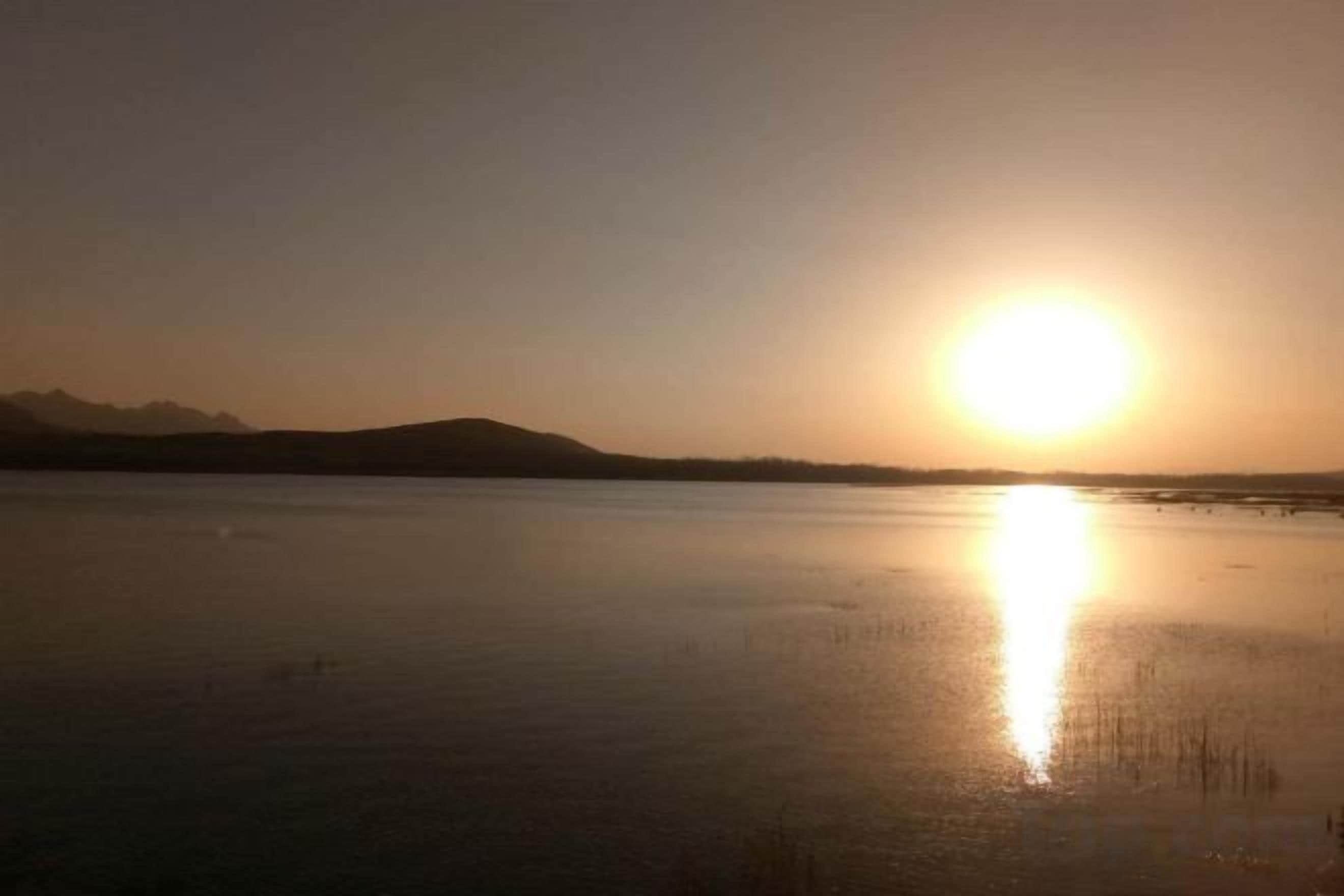 A calm body of water reflecting sunlight with a distant mountain range.