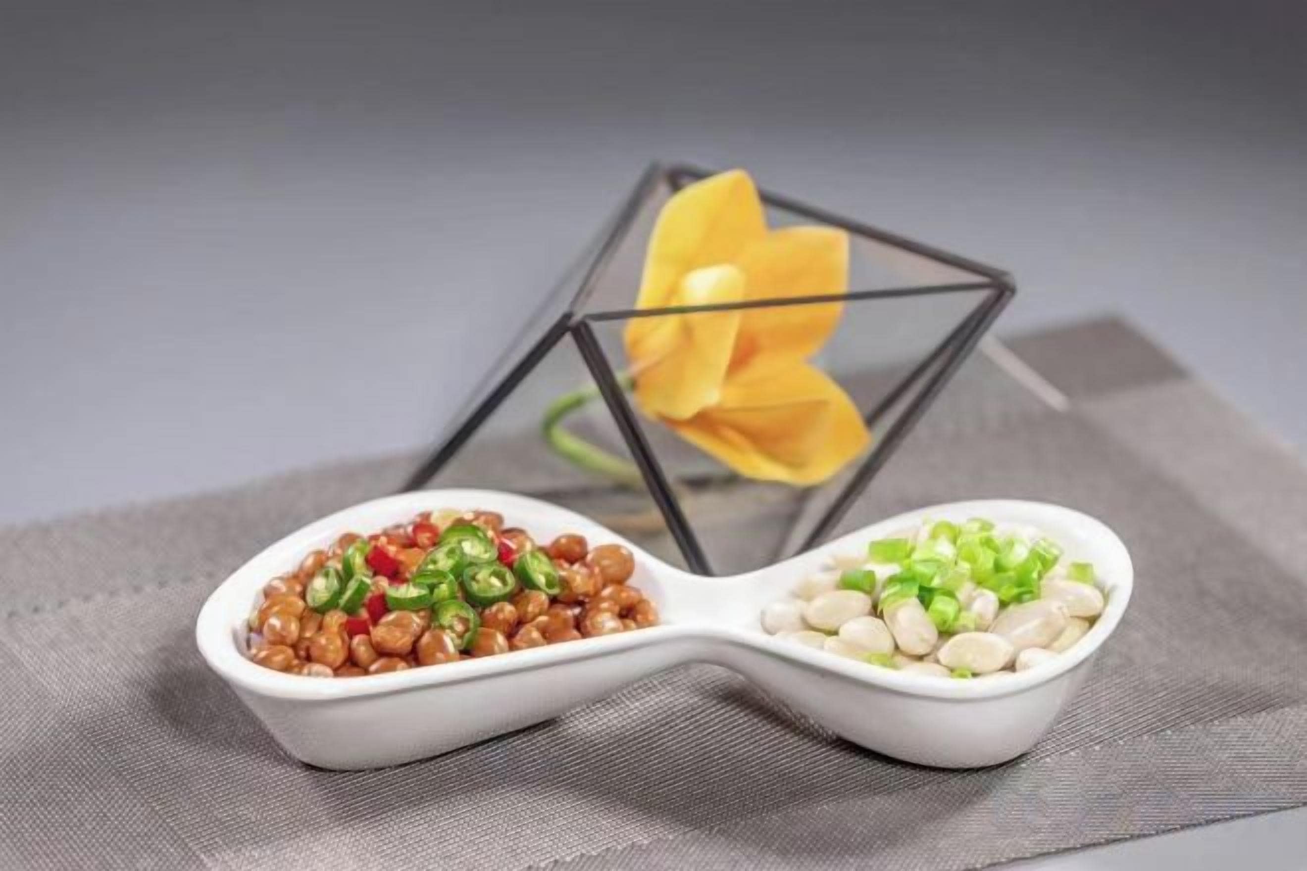 Deux cuillères en céramique blanche, sur lesquelles sont posés des aliments, sur une table.