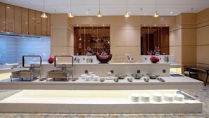 A modern reception area with a central counter displaying various decorative items and a seating area with a large vase and a mirror. - Mingdu Hotel (Wuyang)