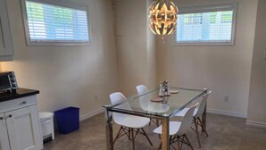 A dining area with a glass table, white chairs, a blue trash bin, and a kitchen area with a microwave. - Spacious 2 BR, 3 Beds, Sleeps 6, Kitchen, Laundry (Richmond Hill)