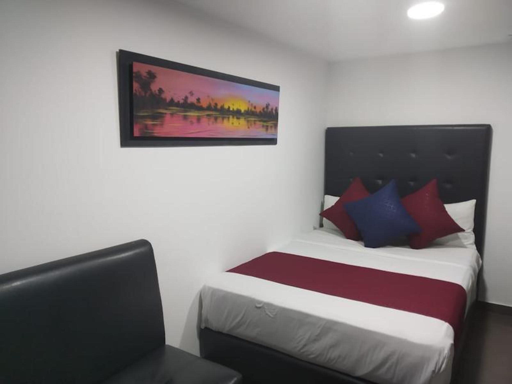 Una habitación de hotel con una cama, cabecera, un cuadro de un atardecer y una silla.