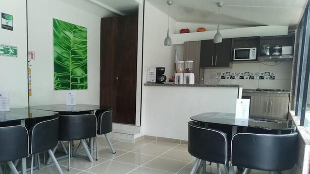A modern kitchen with a microwave, coffee maker, and cabinets. There is a dining area with a table and chairs. - Hotel American Visa Bogota (Bogotá)