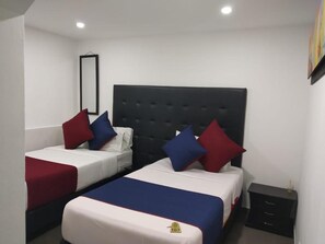 A hotel room with two beds, each with a headboard and pillows. There is a small bedside table and a nightstand with a lamp. - Hotel American Visa Bogota (Bogotá)