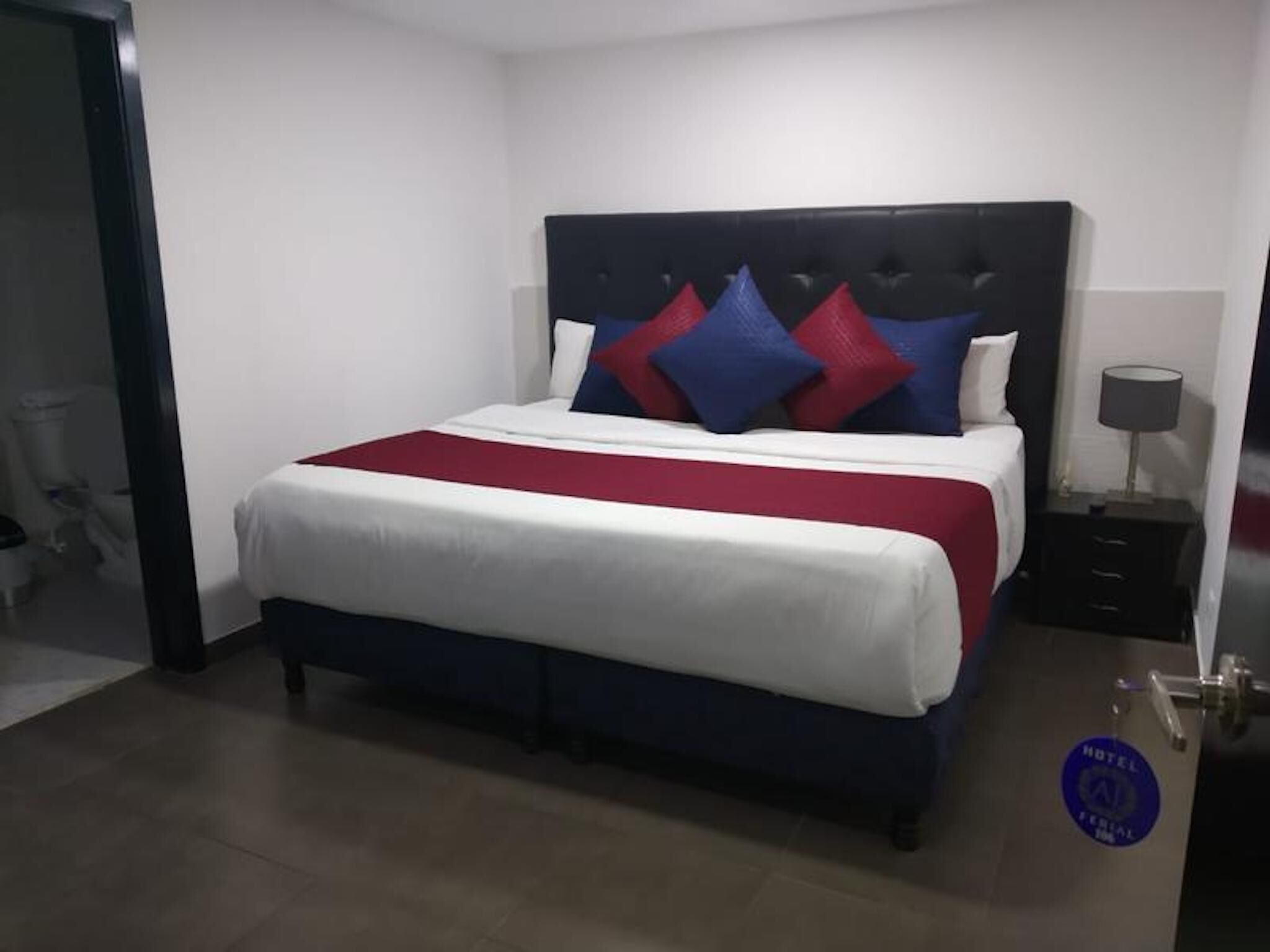 A hotel room with a large bed, a headboard, a nightstand, and a door.