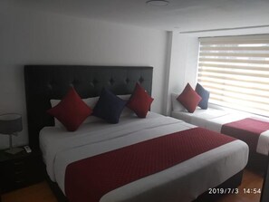 Une chambre d’hôtel avec deux lits, une grande tête de lit et une fenêtre avec des stores.