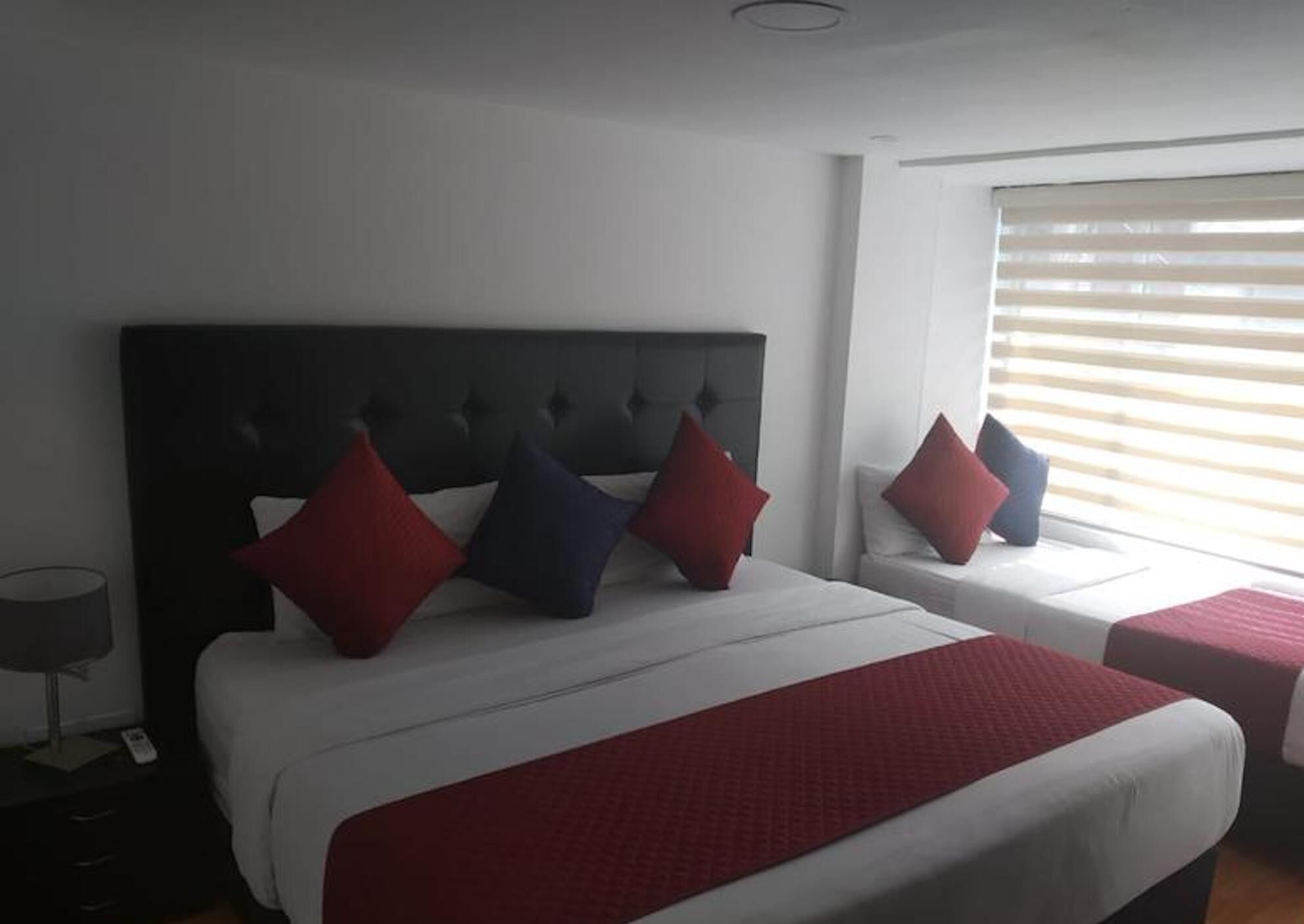 A hotel room with a large bed, a smaller bed, and a window with blinds.