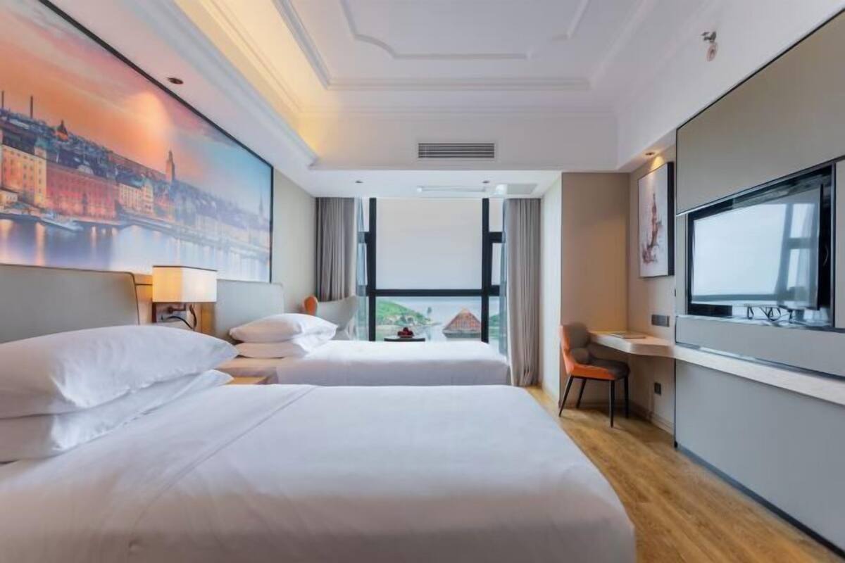 A hotel room with two beds, a desk, a television, and a large window.