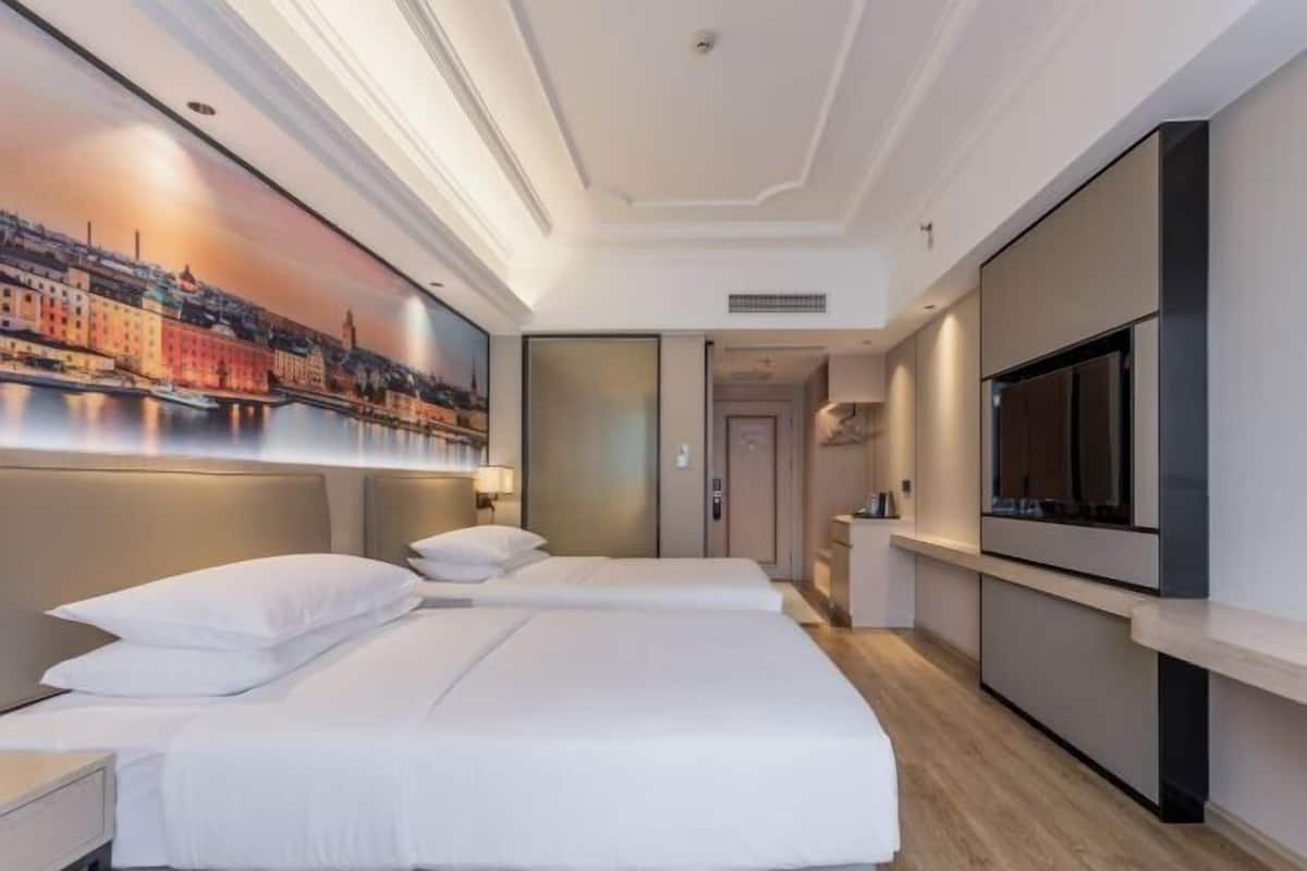 A hotel room with two beds, a large TV, and a cityscape mural on the wall.