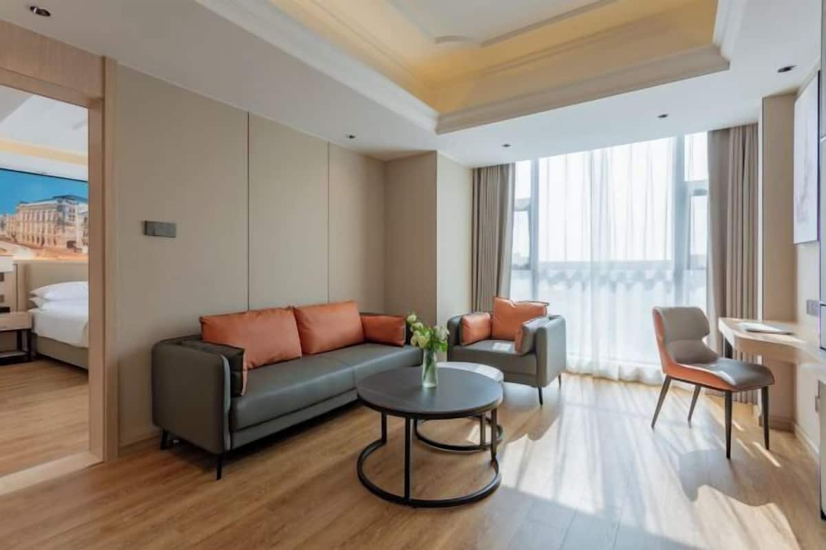 A modern hotel room with a large sofa, a round coffee table, and a desk with a chair.