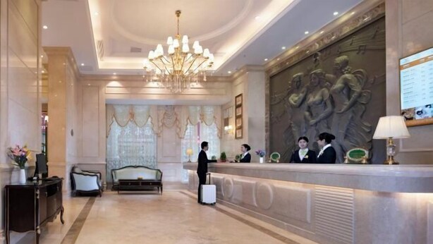 A hotel lobby with a reception desk, a chandelier, a sofa, and a statue on the wall.