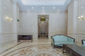 A spacious lobby with a marble floor, a sofa, a console table, and a chandelier.