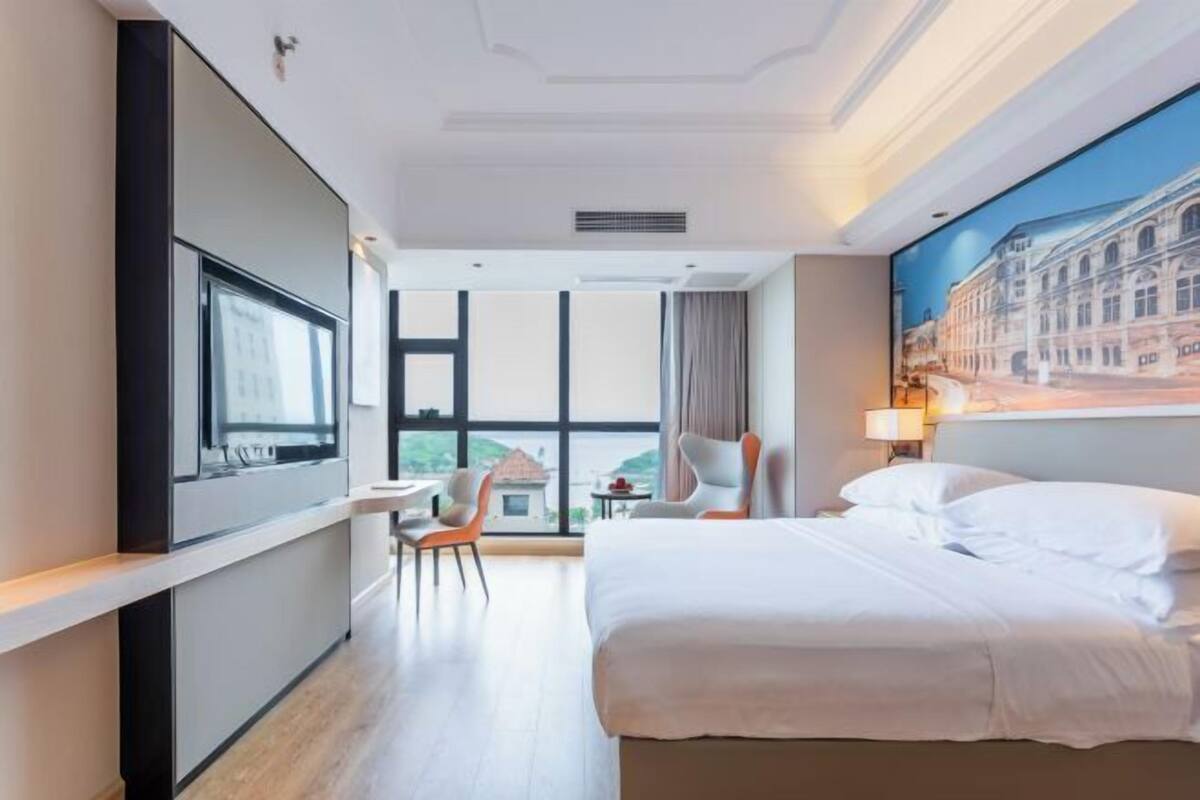 A hotel room with a bed, a desk, a chair, a TV, and a large window.