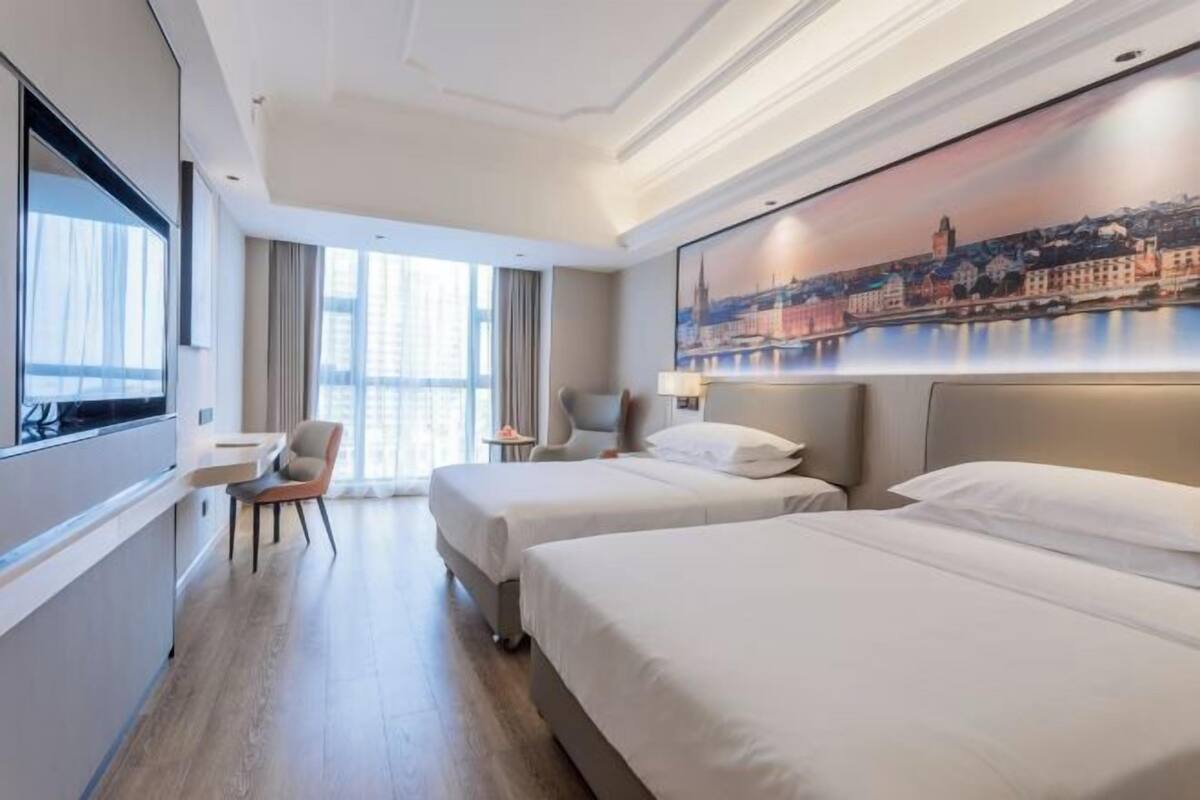 A hotel room with two beds, a desk, a chair, and a large window.