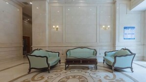 A lobby with three upholstered armchairs and a central ottoman, a patterned carpet, and wall-mounted lighting fixtures.