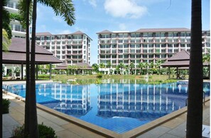 A swimming pool with a tiled deck, surrounded by palm trees and a building with multiple balconies in the background.
