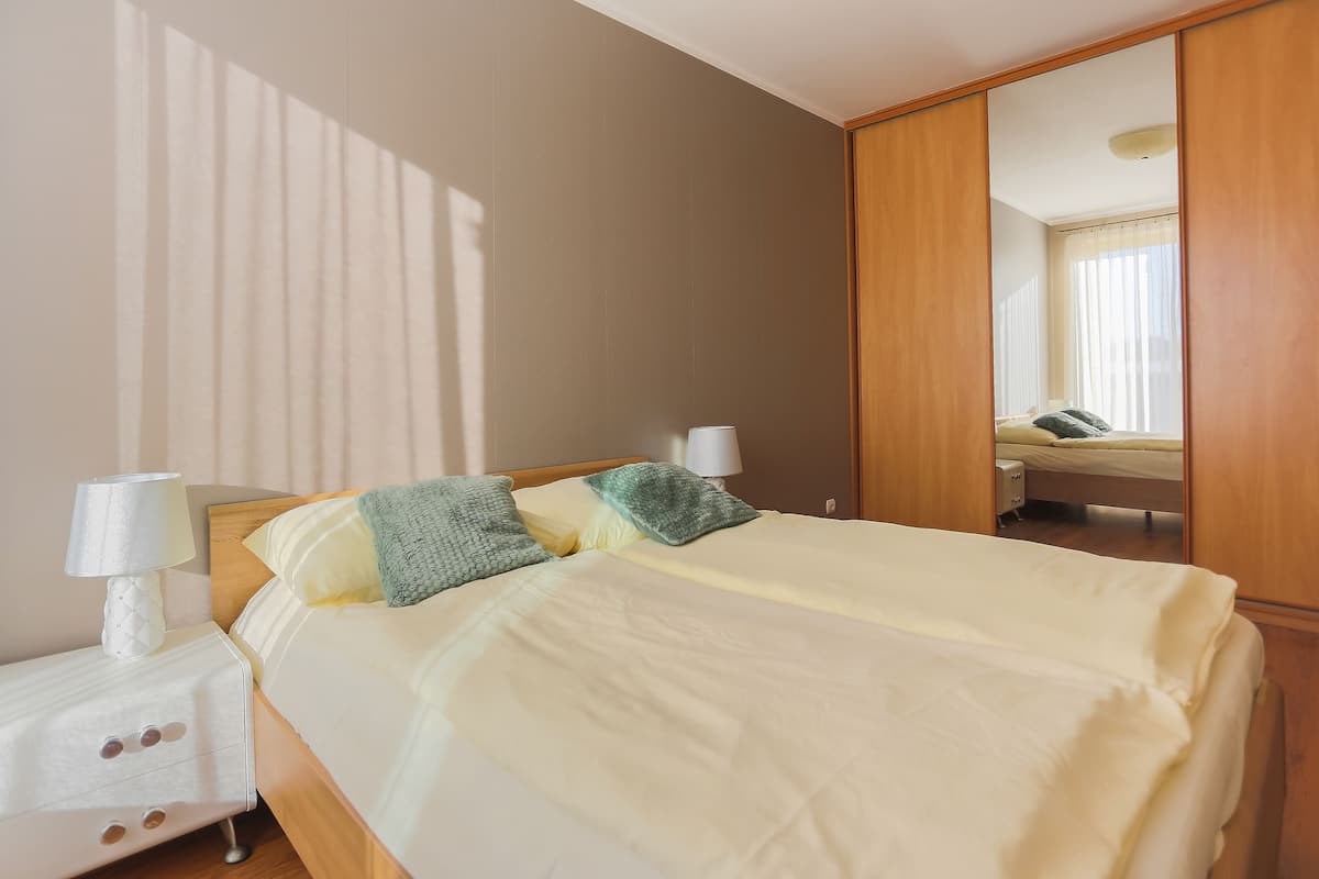 A neatly made bed with a white comforter and two pillows, a bedside lamp, and a wooden nightstand.