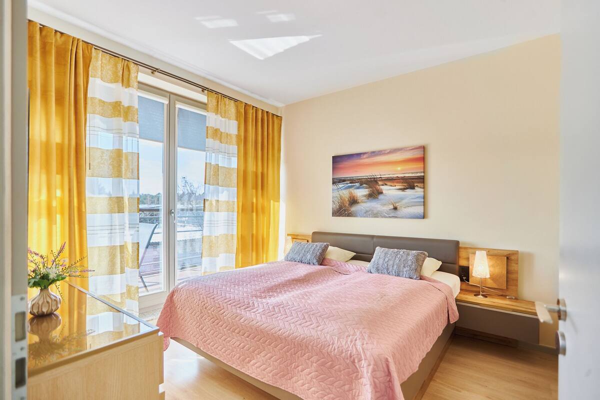 A modern bedroom with a large bed, a nightstand, a lamp, and a painting on the wall.