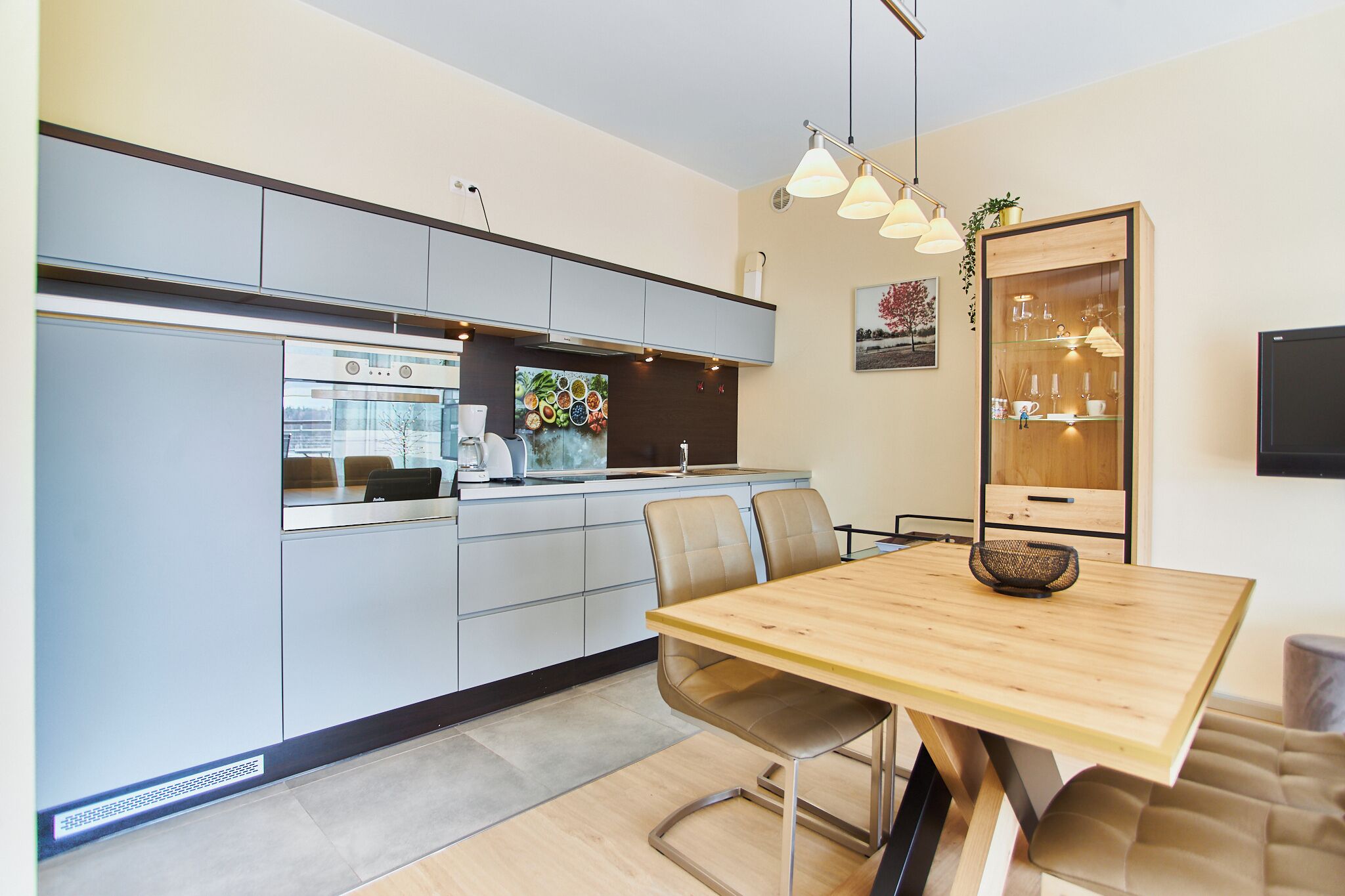 A modern kitchen with integrated appliances, a dining area with a wooden table and chairs, and a built-in cabinet with glass doors.