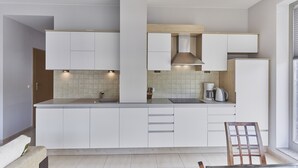 Una cocina moderna con armarios blancos, horno empotrado y cafetera.