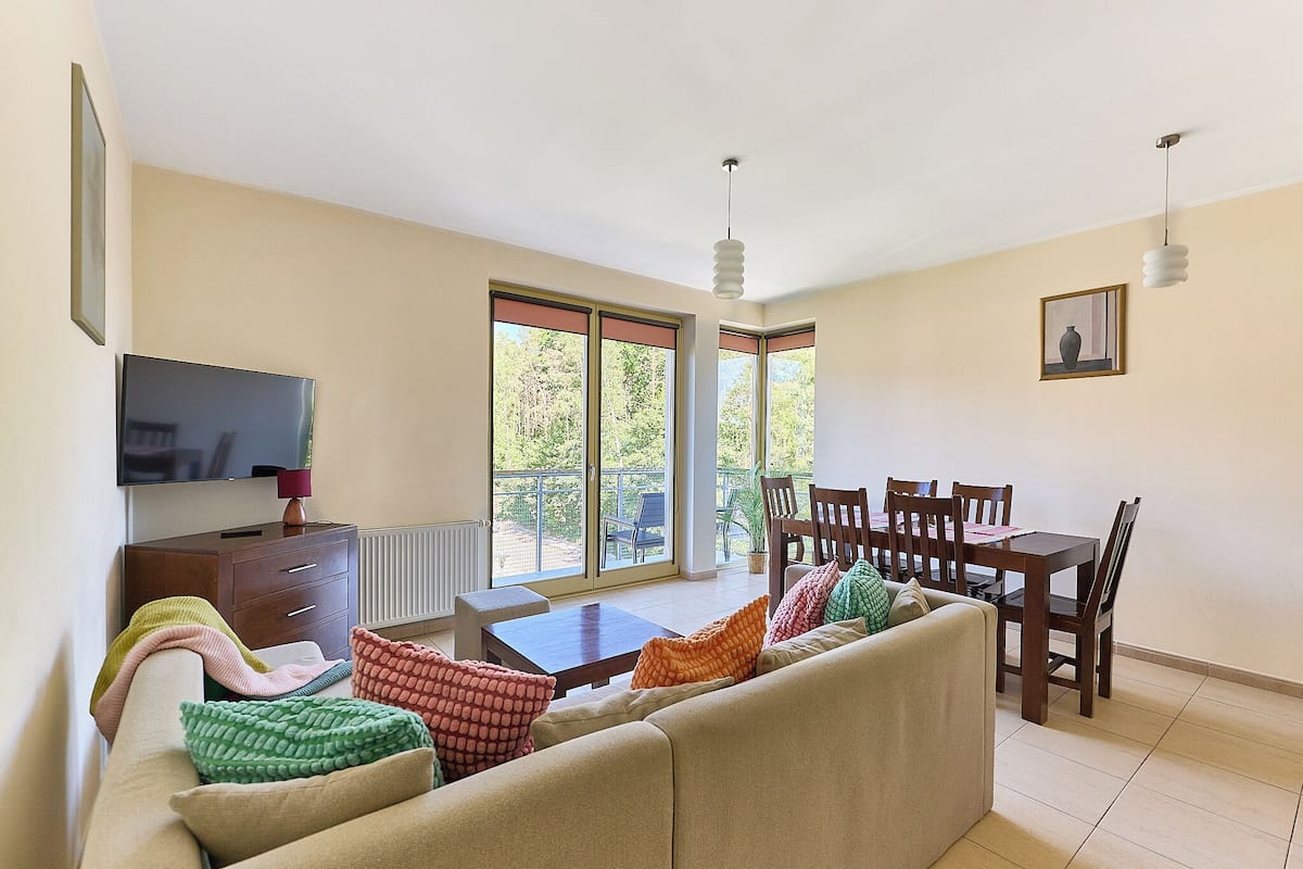 A living room with a sofa, coffee table, TV, and dining area with chairs and a table.