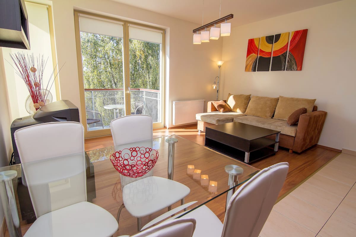 A modern living room with a glass coffee table, white chairs, a sofa, and a painting on the wall.