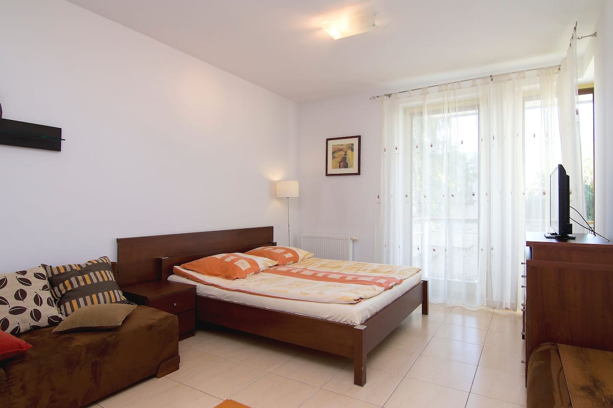 A bedroom with a bed, a wooden dresser, a nightstand, a sofa, and a television.