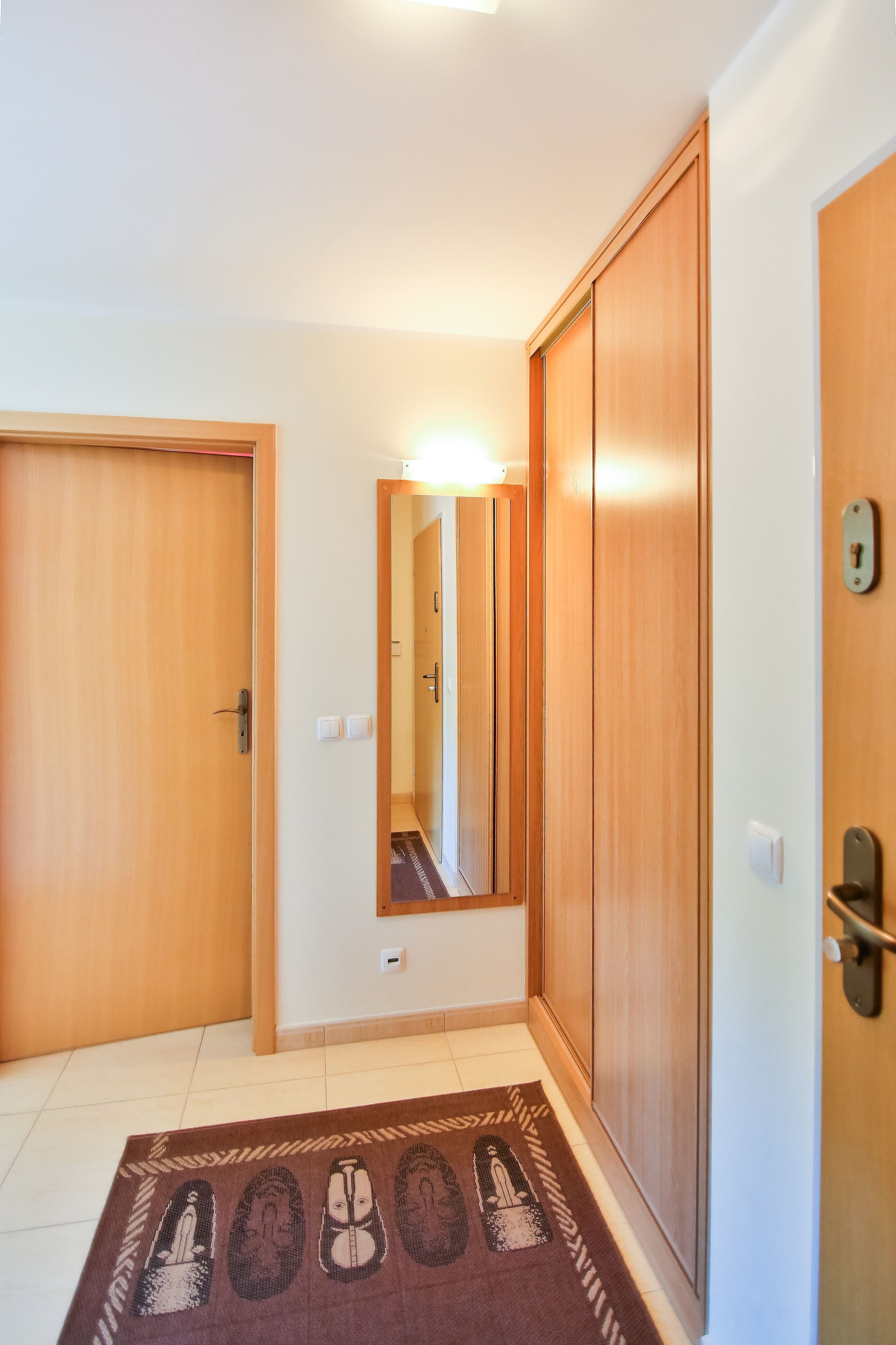 A hallway with wooden doors, a mirror, and a patterned rug.