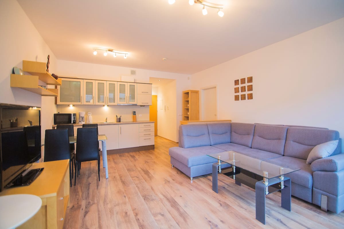 A modern living room with a grey sofa, a glass coffee table, and a dining area with a yellow table and chairs.