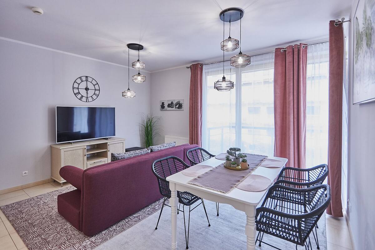 A modern living room with a sofa, dining table, chairs, a TV, and pendant lights.