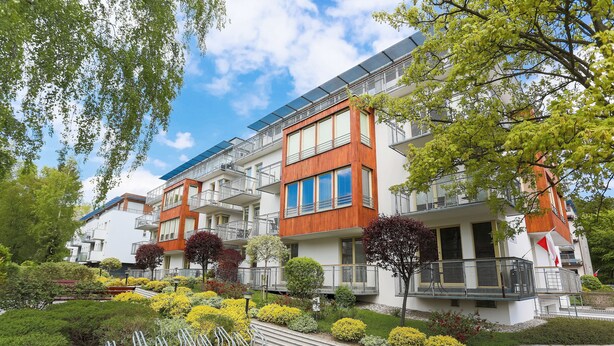 Un moderno edificio de apartamentos con balcones, paneles solares y jardines ajardinados.