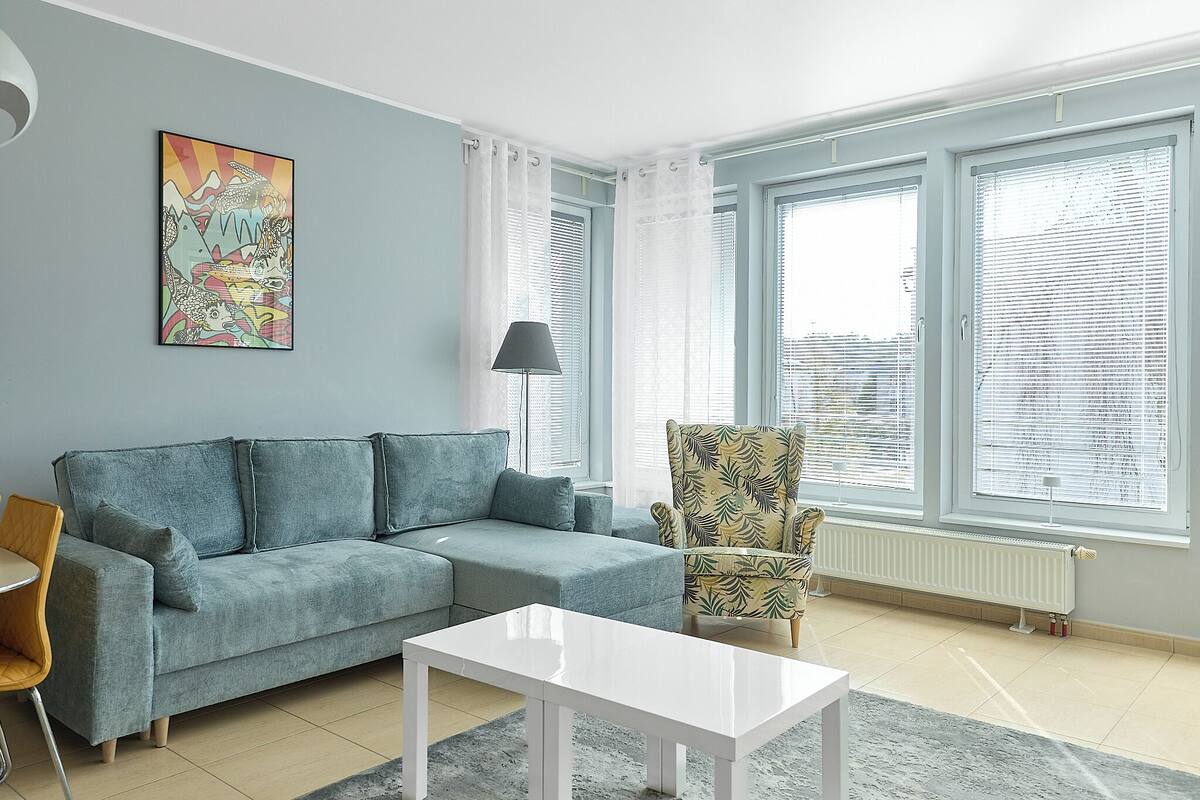 A living room with a sofa, a chair, a coffee table, a radiator, and a window with blinds.