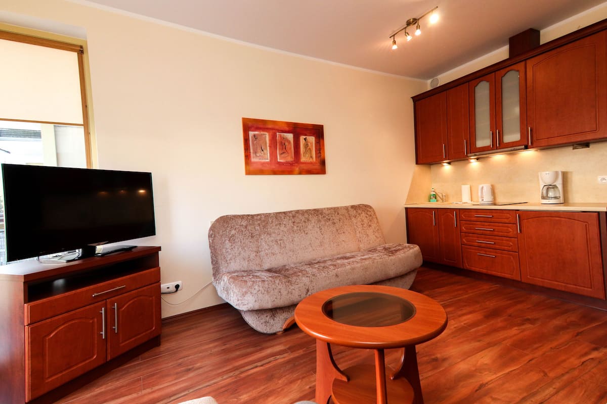 A compact living space with a flat-screen TV on a wooden cabinet, a sofa, a small round table, and wooden cabinets.