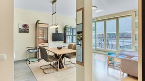 Una sala de estar moderna con un ventanal grande, un comedor con mesa de madera y una cocina con televisor y armarios.
