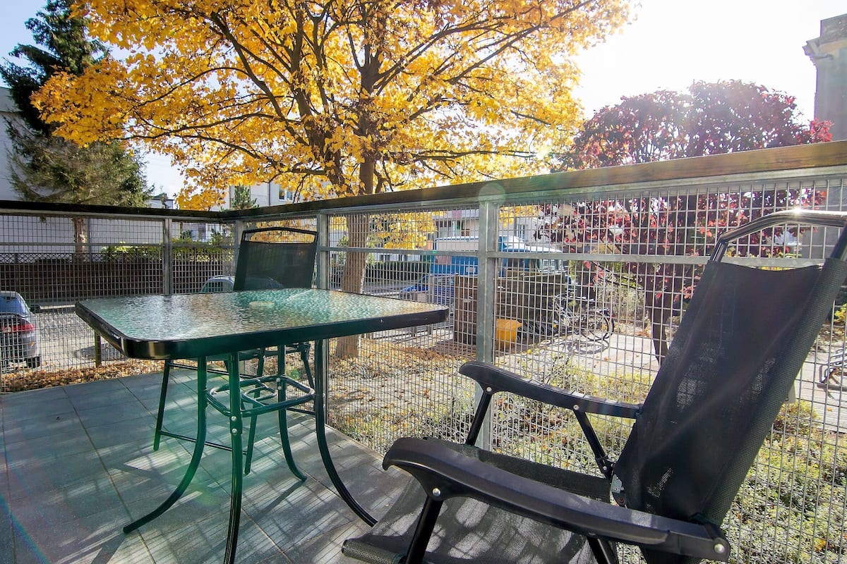 An outdoor patio with a glass table and chairs, surrounded by a metal fence.