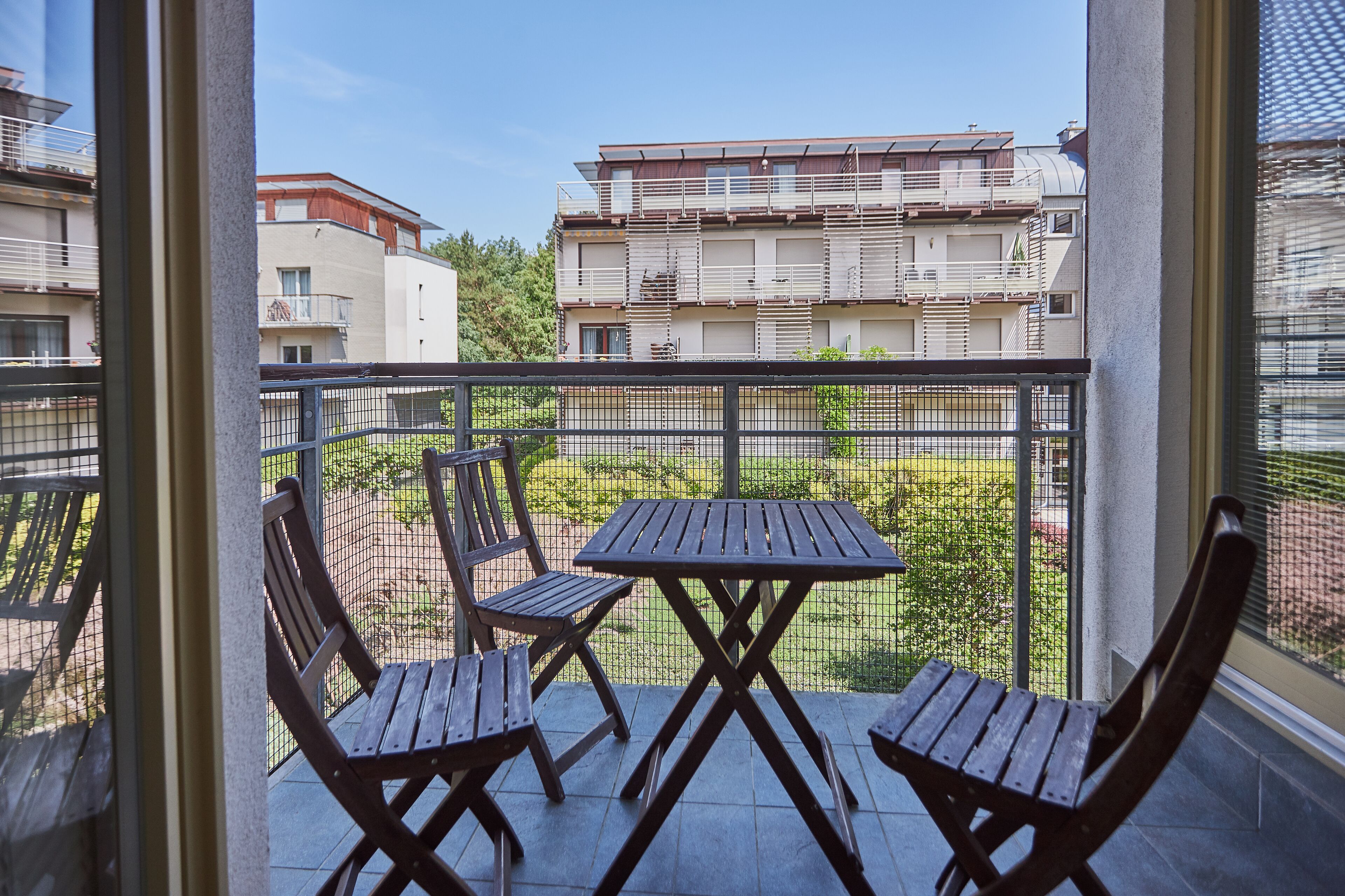Ein Balkon mit Tisch und Stühlen, einem Metallgeländer und Blick auf benachbarte Gebäude.