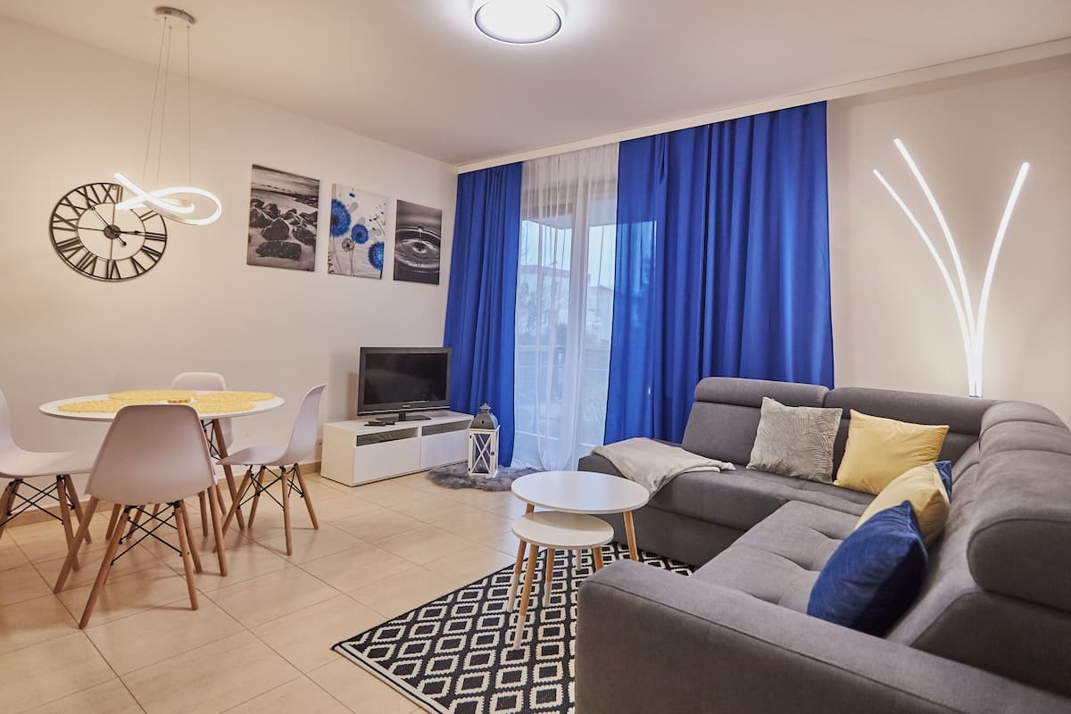 A modern living room with a grey sofa, a dining table with chairs, a TV, and artwork on the wall.