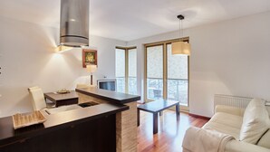 Una sala moderna con un sofá, una zona de comedor con mesa y sillas, una cocina con estufa y ventanas amplias que dejan entrar luz natural.