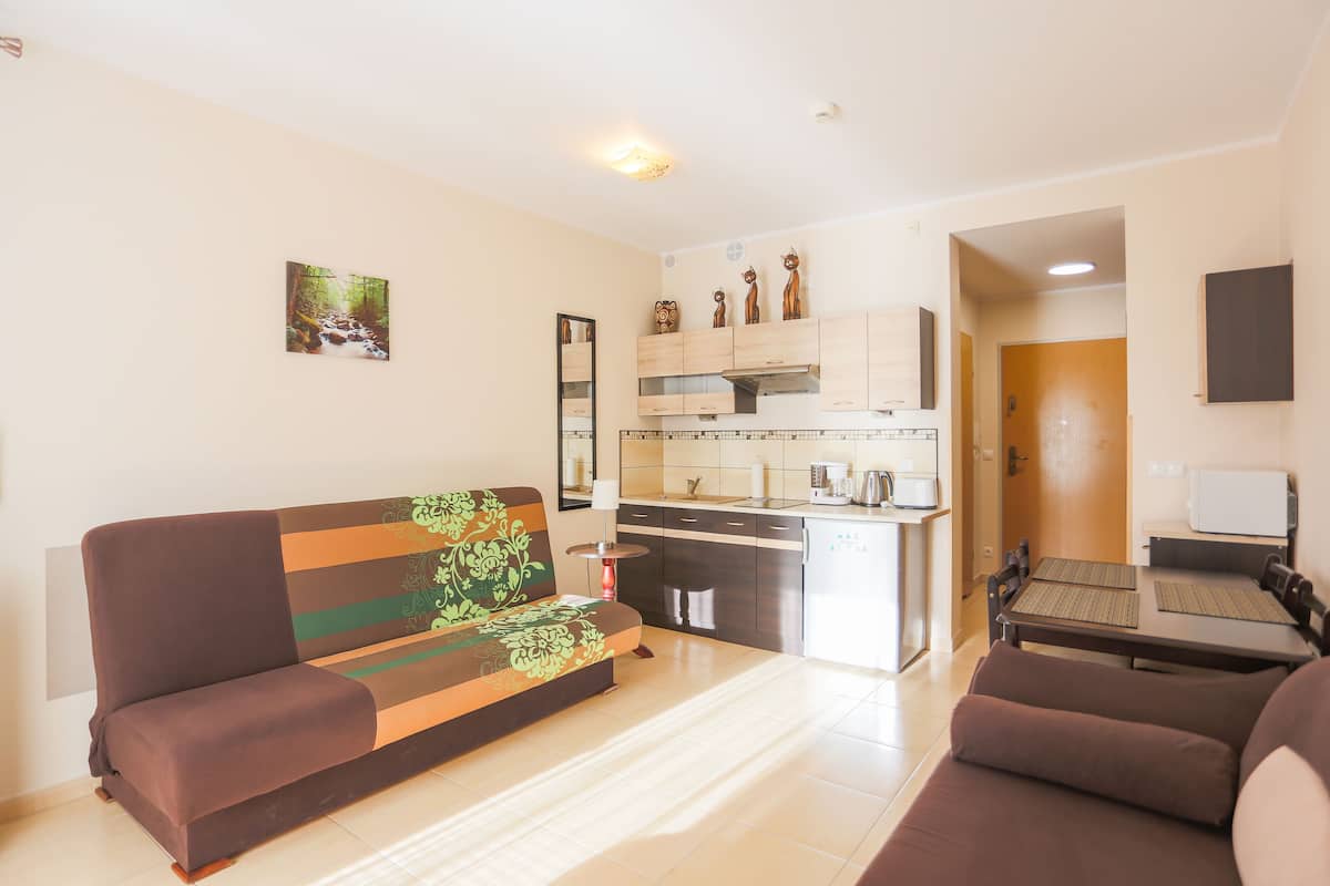 A modern living room with a sofa, a dining table, and a kitchen area with cabinets and a refrigerator.