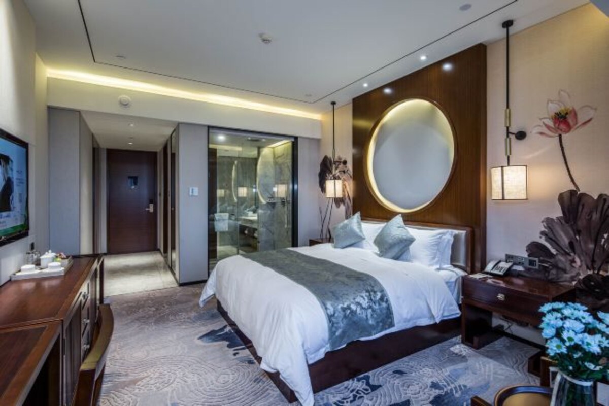 A modern hotel room with a large bed, a bedside table, a mirror, and a view of the hallway.
