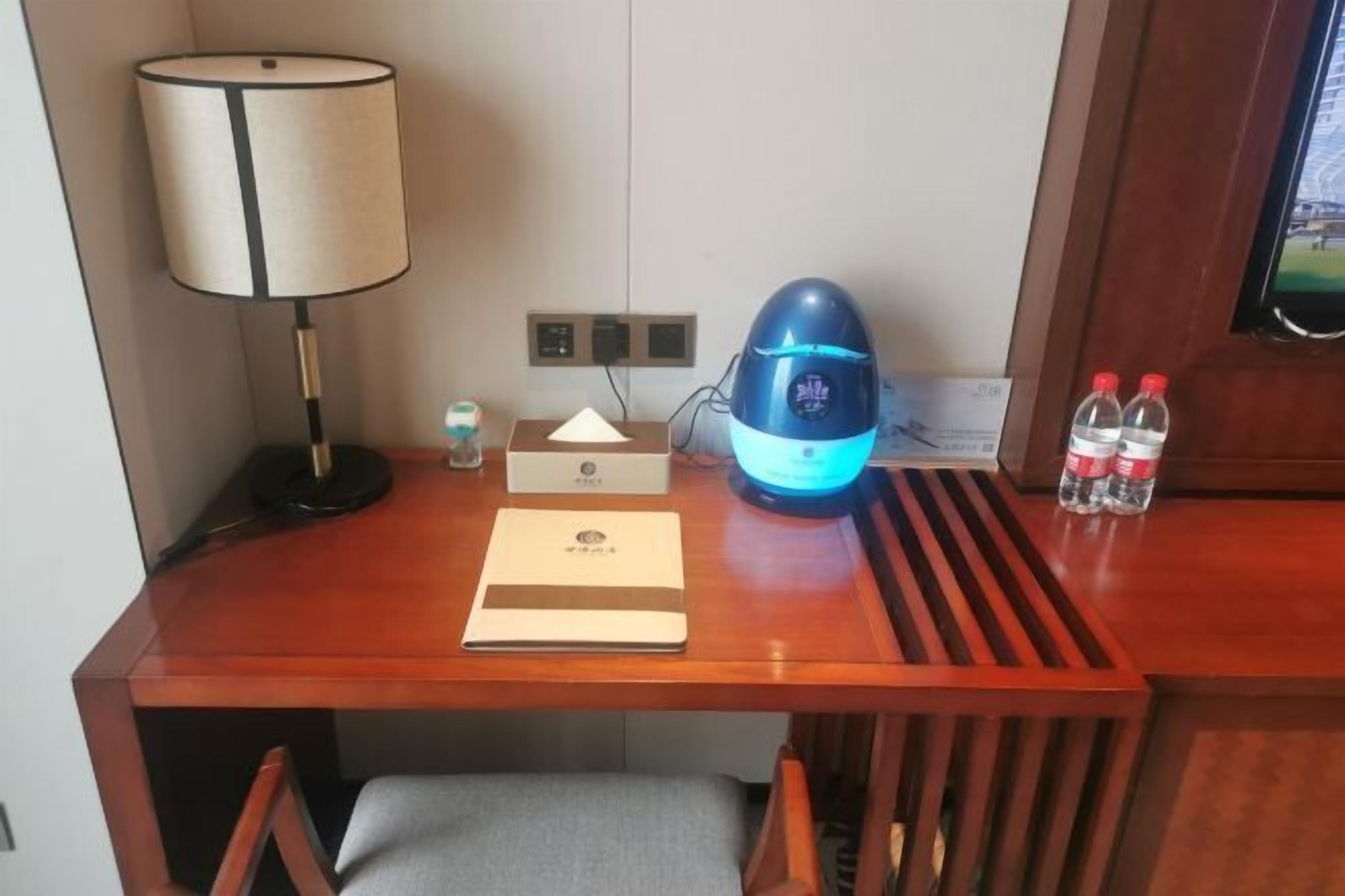 Een houten bureau met een lamp, een blauw apparaat, een waterfles en een klein flesje.