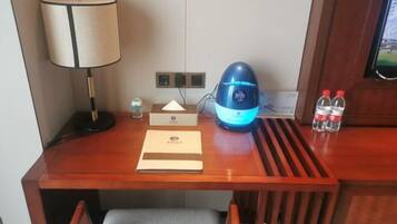 Een houten bureau met een lamp, een blauw apparaat, een waterfles en een klein flesje.