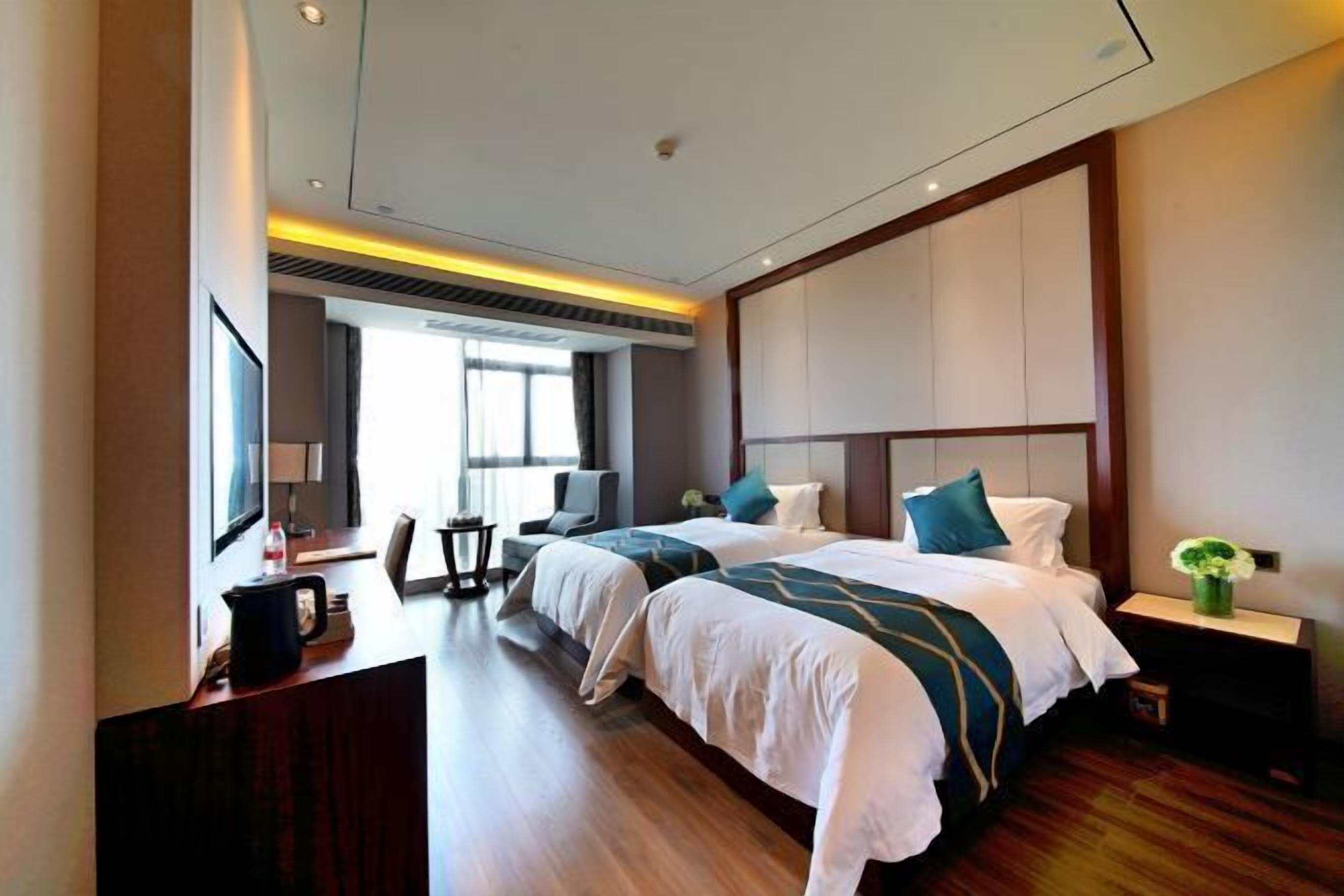A hotel room with two beds, a desk with a chair, a TV, and a window.