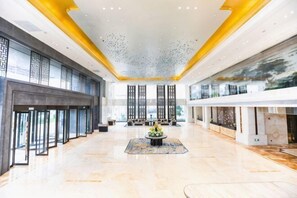 Eine großzügige Lobby mit hoher Decke, einer zentralen Sitzecke und großen Fenstern.