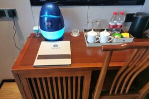 A wooden table with a laptop, a blue kettle, a tray with a teapot, cups, and bottled water. - Expo Hotel (Tongxiang)