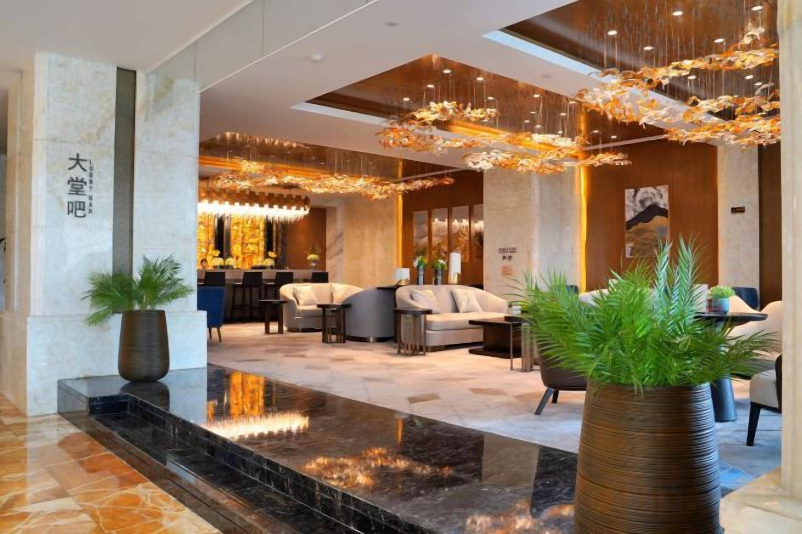 A hotel lobby with a reception desk, seating area, and a large potted plant.