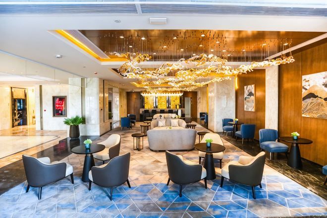 A hotel lobby with a chandelier, sofas, and round tables.