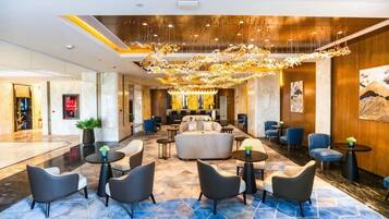 A hotel lobby with a chandelier, sofas, and round tables.