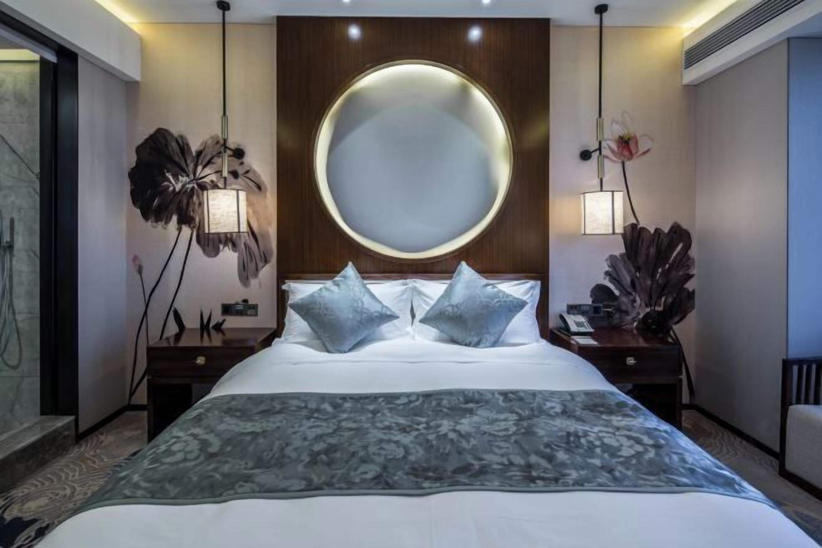 A hotel room with a large bed, two nightstands, a round mirror, and a floral wall decoration.